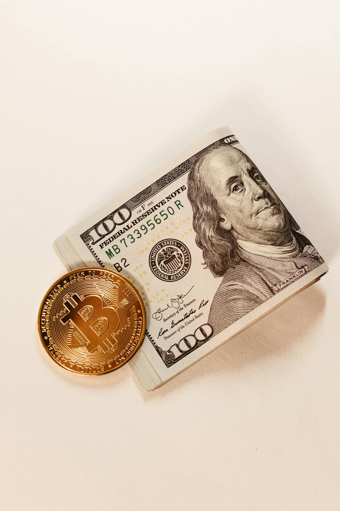Close-up of a Bitcoin coin placed beside a stack of $100 US dollar bills, showcasing cryptocurrency and traditional currency.